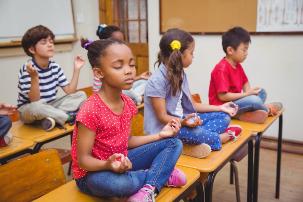 Pupils meditating in lotus position on desk in classroom
