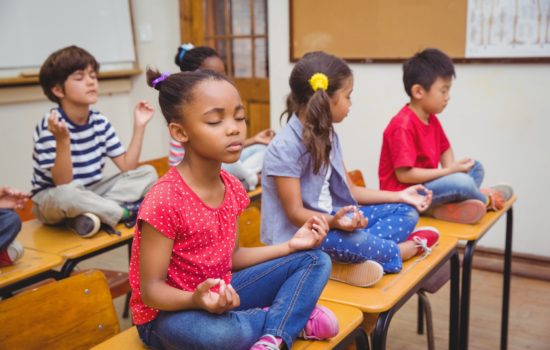 Pupils meditating in lotus position on desk in classroom